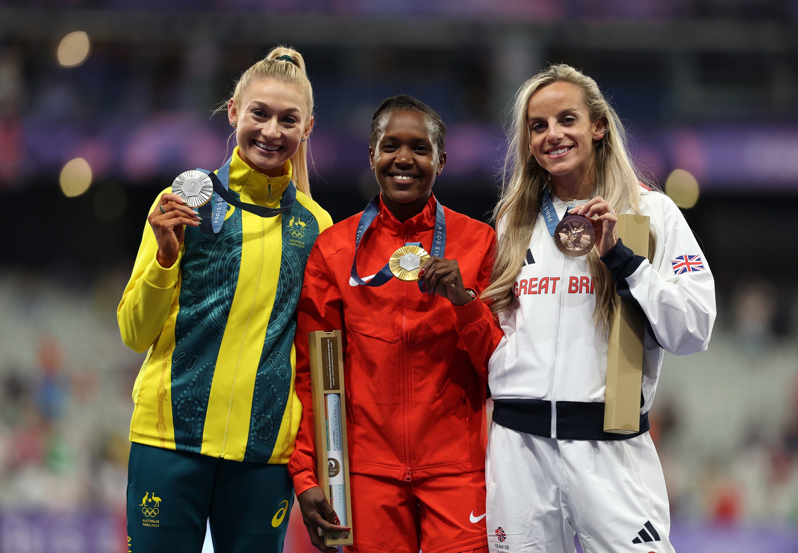 PARIS, FRANCE - AUGUST 10: Gold medalist Faith Kipyegon of Team Kenya (C), Silver medalist Jessica Hull of Team Australia (L) and Bronze medalist Georgia Bell of Team Great Britain (R) celebrate on the podium during the Women's 1500m medal ceremony on day fifteen of the Olympic Games Paris 2024 at Stade de France on August 10, 2024 in Paris, France. (Photo by Al Bello/Getty Images)